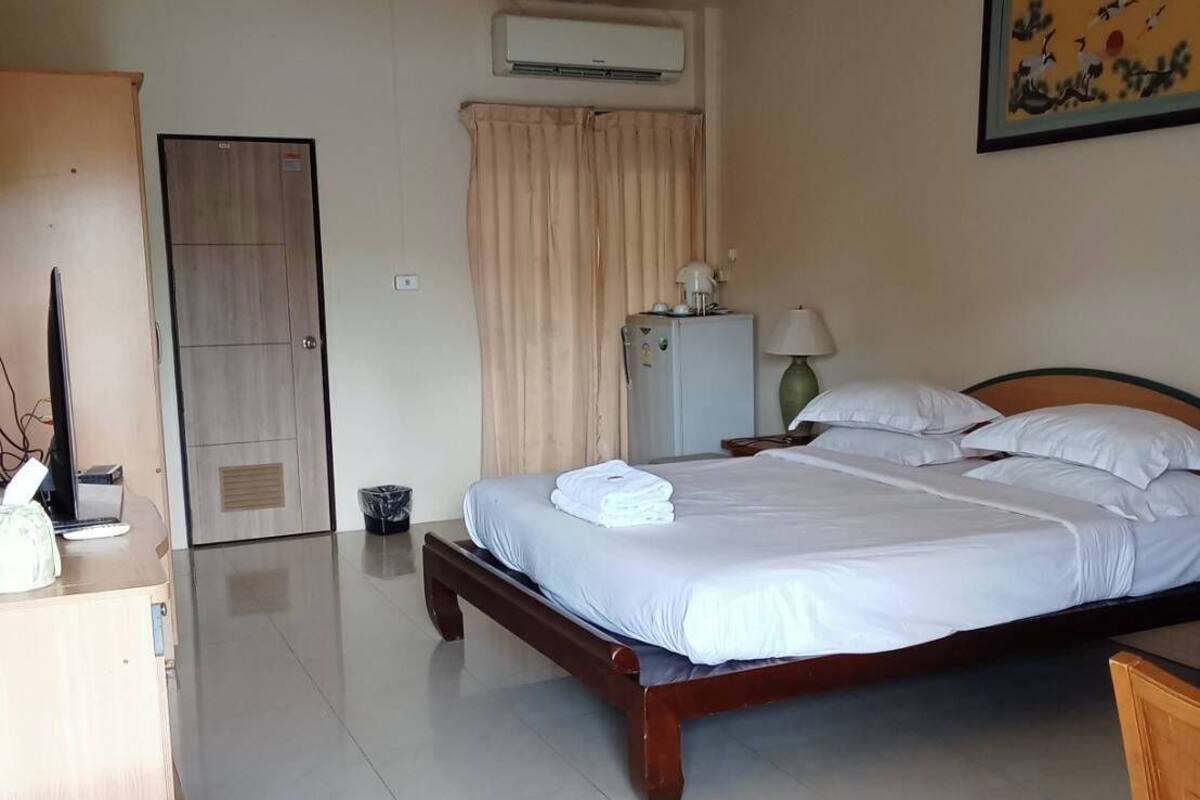 A hotel room with a bed, a desk, a chair, an air conditioning unit, a door, and a curtain.