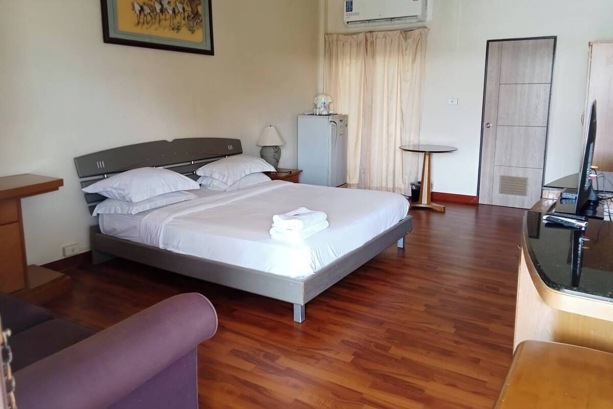A hotel room with a bed, a desk, a chair, an air conditioner, and a television.
