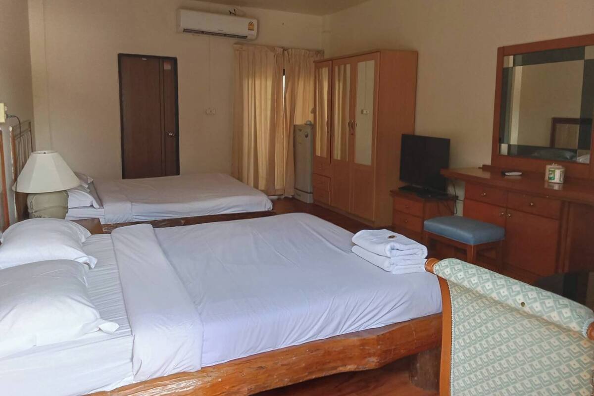 A hotel room with two beds, a TV, a desk with a mirror, and an air conditioning unit.