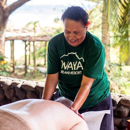A person receiving a massage in a natural setting with a stone wall and greenery in the background.