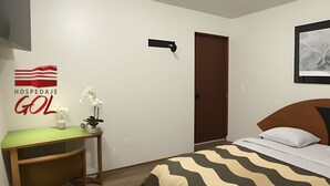 Habitación de hotel con cama, escritorio, silla, una pequeña mesa con un jarrón de flores y un cuadro colgado en la pared.