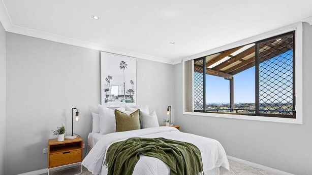 A bedroom with a bed, a nightstand, a window with a view, and a framed picture on the wall. - Ocean-View Retreat for Family Getaways
 (Cringila)