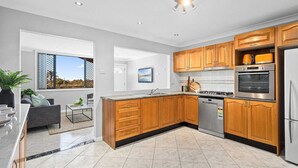 A modern kitchen with wooden cabinets, stainless steel appliances, and a large window offering a view. - Ocean-View Retreat for Family Getaways
 (Cringila)
