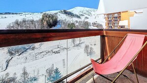 Un balcón con barandilla de madera, una silla roja y vistas a un paisaje montañoso nevado.
