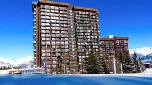 Un hotel de varios pisos con balcones, situado cerca de una masa de agua y montañas.