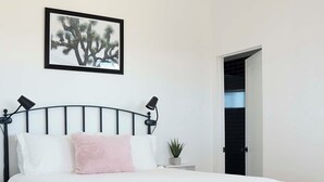 A modern bedroom with a bed, bedside lamps, a small potted plant, and a framed picture on the wall. - New Desert Oasis | Pool, EV Charger, Spa, Short Walk to Joshua Tree Park (Joshua Tree)