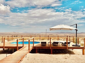 Une terrasse en bois avec une piscine, un espace salon extérieur et une vue sur le paysage désertique.