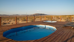 A wooden deck with a swimming pool and hot tub, surrounded by a desert landscape.