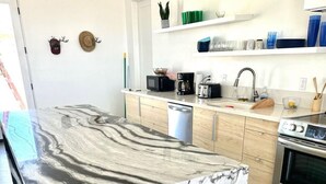 A modern kitchen with a marble countertop, stainless steel appliances, and wooden cabinets. - New Desert Oasis | Pool, EV Charger, Spa, Short Walk to Joshua Tree Park (Joshua Tree)