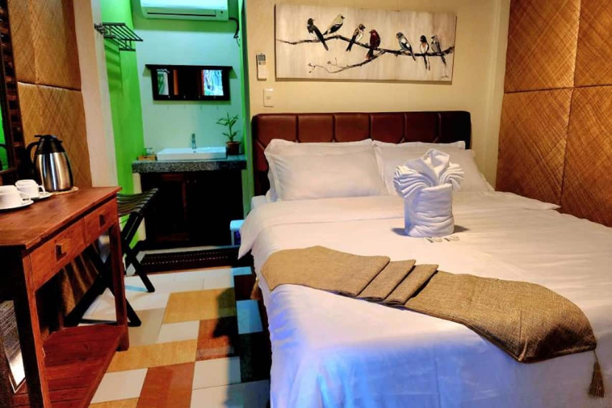 A hotel room with a bed, a desk with a coffee maker, a painting of birds on the wall, and a bathroom visible through an open door.