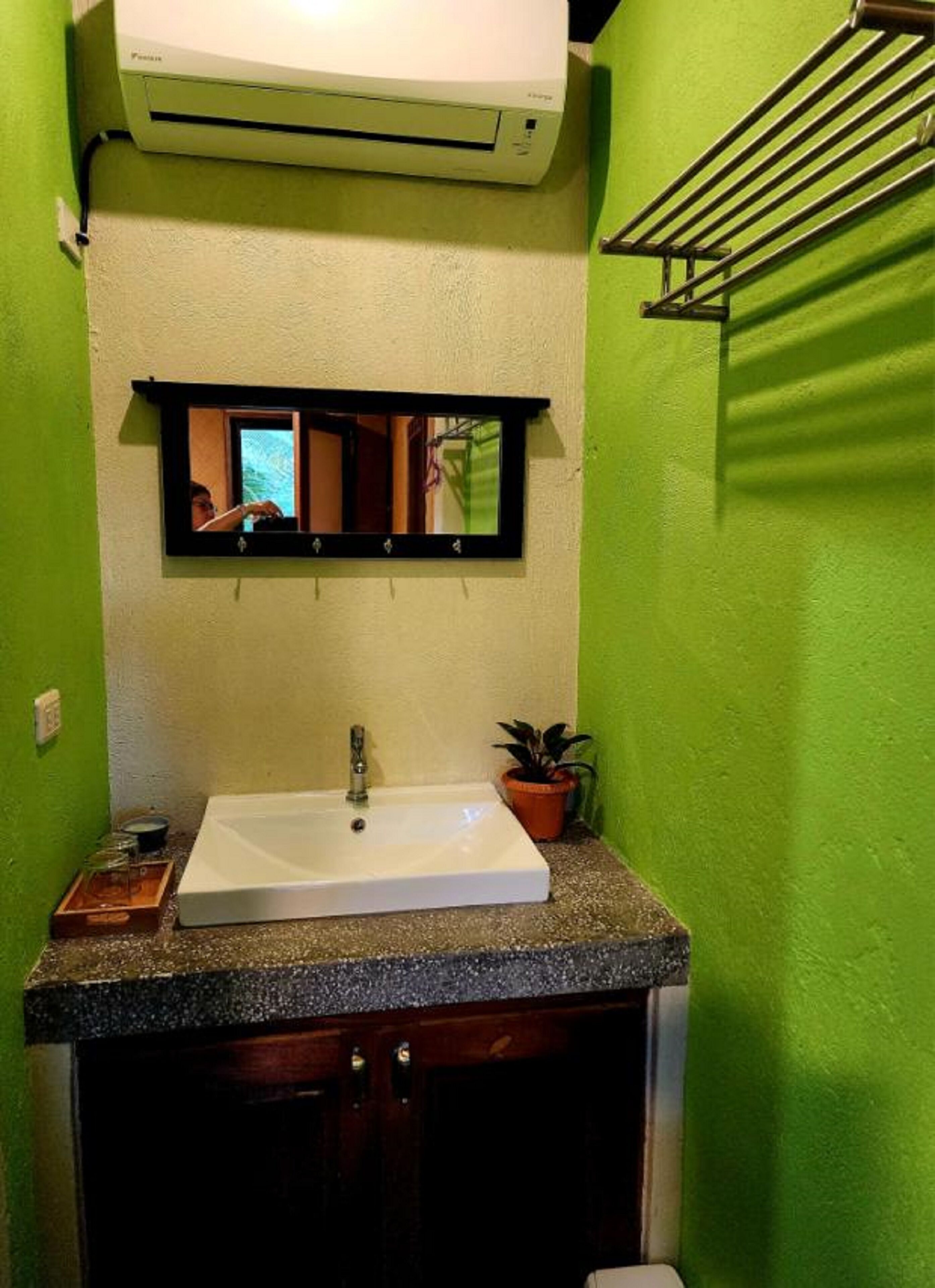 Un baño con un lavamanos blanco, un espejo y una pared verde.