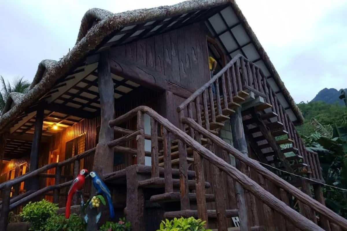 A rustic wooden building with a thatched roof, a wooden staircase, and a small garden area with a bird sculpture.