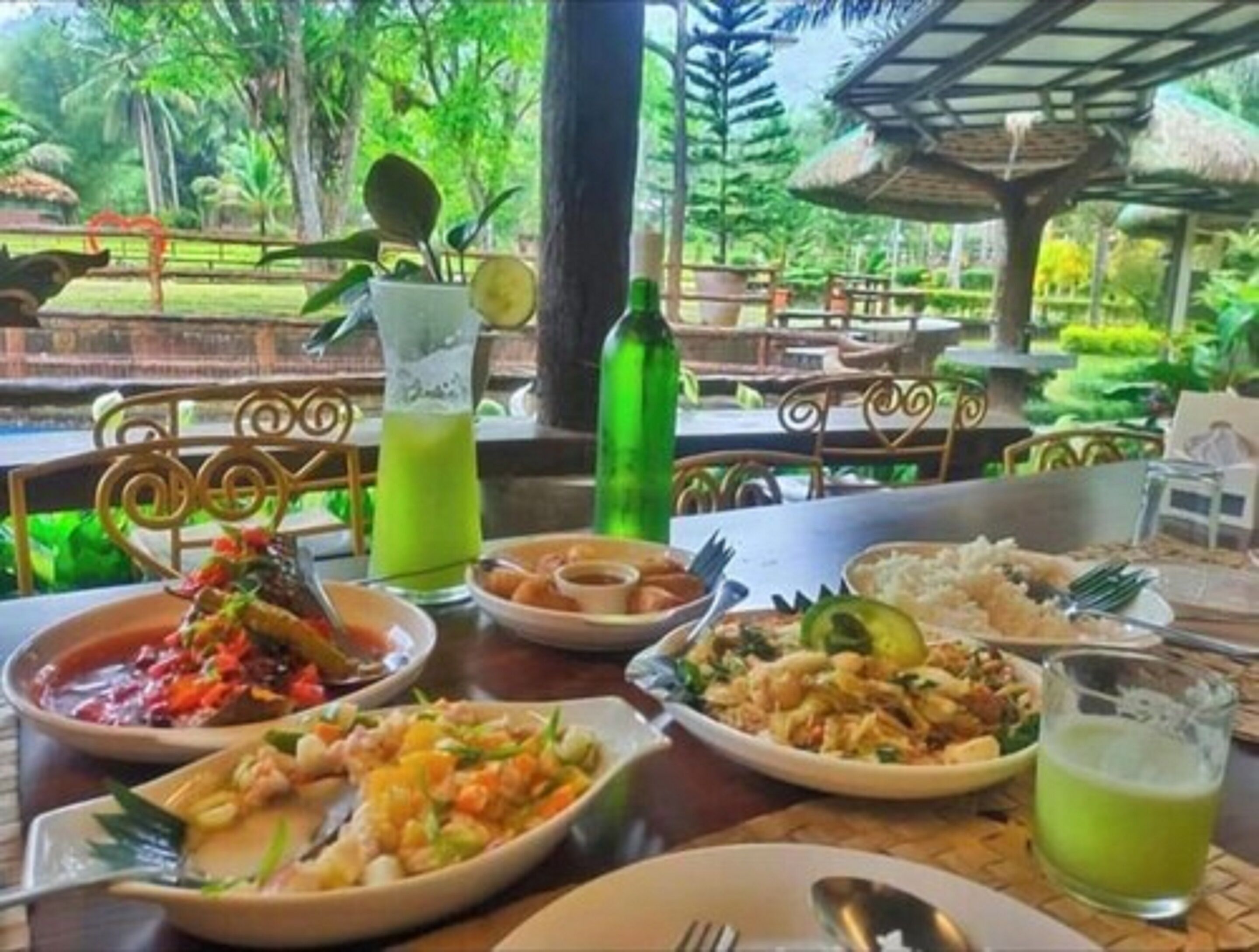 A dining table with various dishes and drinks, surrounded by a lush garden view.