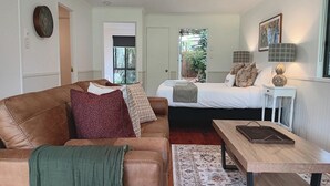 Una sala de estar acogedora con un sofá de cuero marrón, una mesa de centro de madera y una cama con ropa de cama blanca.