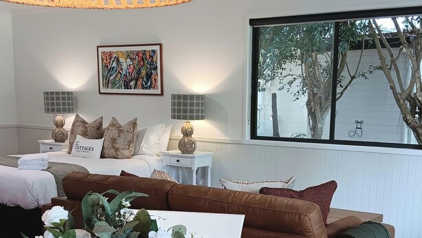 Una sala moderna con un sofá marrón, una mesa de comedor de madera con un florero y un ventanal con vistas a árboles.
