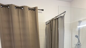 Un área de ducha con mampara de vidrio, cabezal de ducha y perchero.