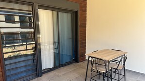 Un balcón con puerta corrediza de vidrio, una mesa de madera y cuatro sillas.