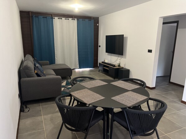 A living room with a sofa, a TV, and a dining area with a table and chairs.