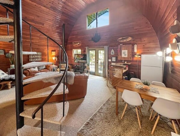 Cozy cabin interior with a high ceiling, spiral staircase, and a dining area with a wooden table and four chairs.