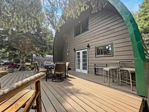 Relax on the outdoor deck with a table and chairs, surrounded by trees and a covered area.