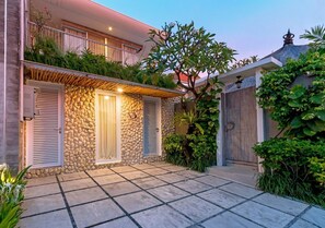 A two-story house with a stone facade, a balcony, and a paved patio area. - 2 Bedroom Villa In Seminyak With Private Pool (Bali)