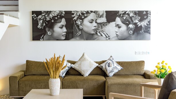 Ein Wohnzimmer mit einem braunen Sofa, einer weißen Vase mit Trockenpflanzen und einem Gemälde über dem Sofa.