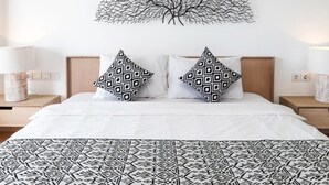 Ein Schlafzimmer mit einem Bett, zwei Kissen mit Muster, einem Baumgemälde an der Wand und Nachttischlampen.