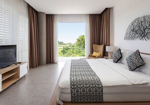 A hotel room with a large bed, a TV on a wooden stand, a balcony with curtains, and a view of greenery. - 2 Bedroom Villa In Seminyak With Private Pool (Bali)