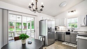 A modern kitchen with white cabinets, stainless steel appliances, and a dining area with a table and chairs. - Quaint Cottage of Holly Springs (Holly Springs)