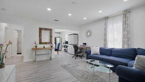 Ein modernes Wohnzimmer mit einem blauen Sofa, einem Glastisch und einem Schreibtisch mit einem Computer.