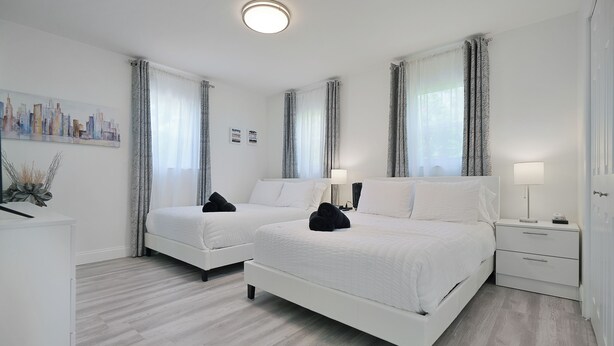 Ein Hotelzimmer mit zwei Einzelbetten, einem Schreibtisch, einem Stuhl, einer Lampe und einem Stadtbild an der Wand.