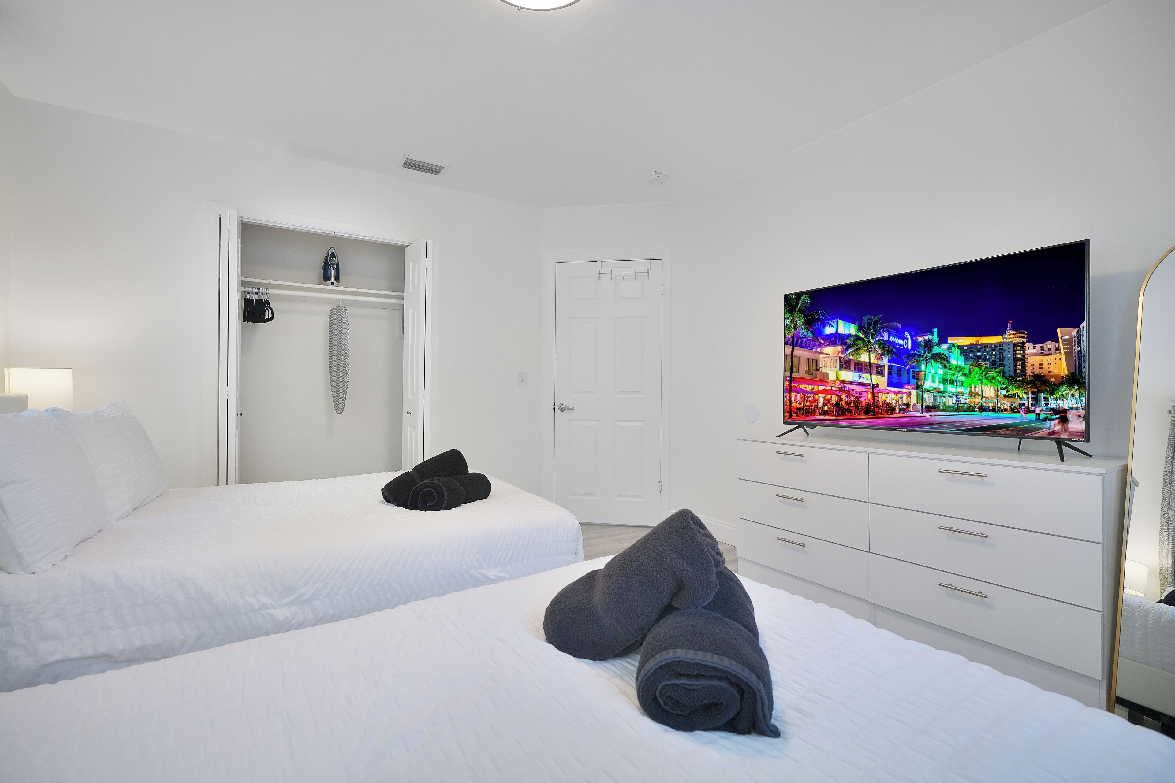 A hotel room with two beds, a TV displaying a cityscape, a wardrobe, and a door.