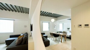 Una sala moderna con un sofá, un comedor con una mesa y sillas, y una cocina al fondo.