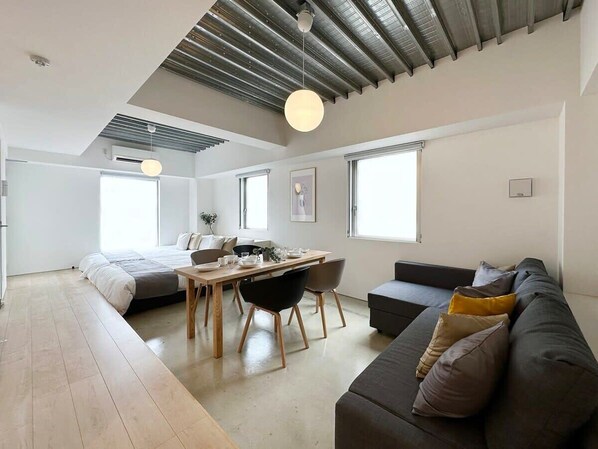 A modern, open-plan living space with a dining area, a sofa, and a bed. - New Studio Apt in the City Center for 6Ppl (Naka Ward, Hiroshima)