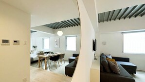 A modern living room with a black sofa, a dining area with a table and chairs, and a kitchen in the background.