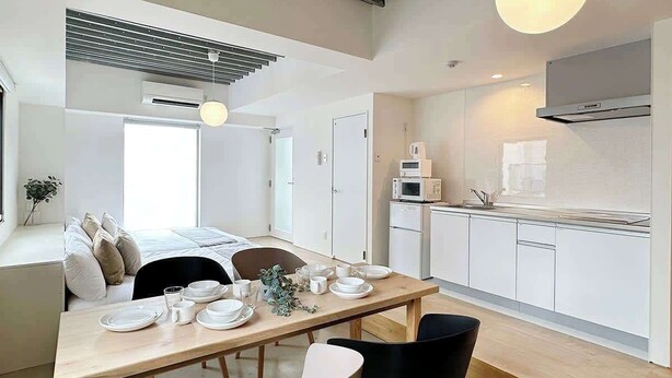 A modern kitchen with white cabinets, a dining table with chairs, and a hanging light fixture.