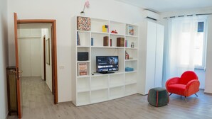 Una sala de estar con un mueble blanco para entretenimiento, un televisor de pantalla plana y un sillón rojo.