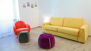 Una habitación con un sofá amarillo, un sillón rojo y un reposapiés morado.