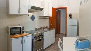 Una cocina compacta con armarios blancos, microondas, estufa y tostadora.