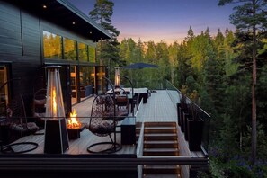 A modern outdoor deck with a fire feature, seating, and a view of a forest.