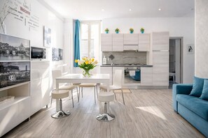 Una cocina moderna con armarios blancos, una cortina azul y un jarrón con tulipanes sobre la mesa de comedor.