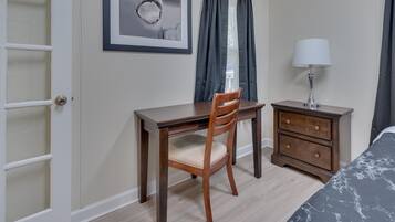 Een slaapkamer met een bed, een houten bureau, een stoel, een nachtkastje en een lamp.