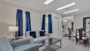 Ein modernes Wohnzimmer mit grauem Sofa, einem Couchtisch und einem Essbereich mit Holztischen und -stühlen.
