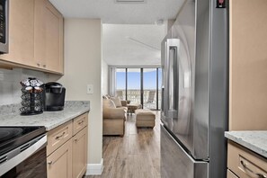 A modern kitchen with a stainless steel refrigerator, a coffee machine, and a dining area with a view.