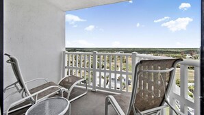 Un balcon avec deux chaises et une table, une balustrade blanche et une vue sur un paysage lointain.