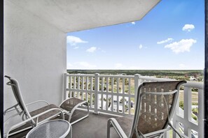 A balcony with two chairs and a table, a white railing, and a view of a distant landscape.