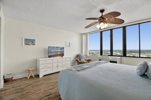 A bedroom with a large bed, a ceiling fan, a TV, a chair, and a view of the landscape.