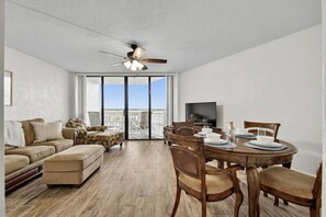 A modern living room with a sofa, dining table, chairs, a ceiling fan, and a TV.
