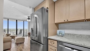 Une cuisine moderne dotée d’appareils électroménagers en acier inoxydable, de meubles en bois et d’une grande porte-fenêtre coulissante donnant sur un balcon.