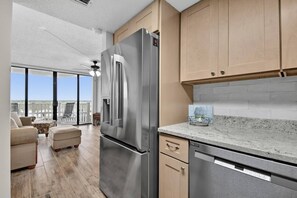 A modern kitchen with stainless steel appliances, wooden cabinets, and a large sliding glass door leading to a balcony.